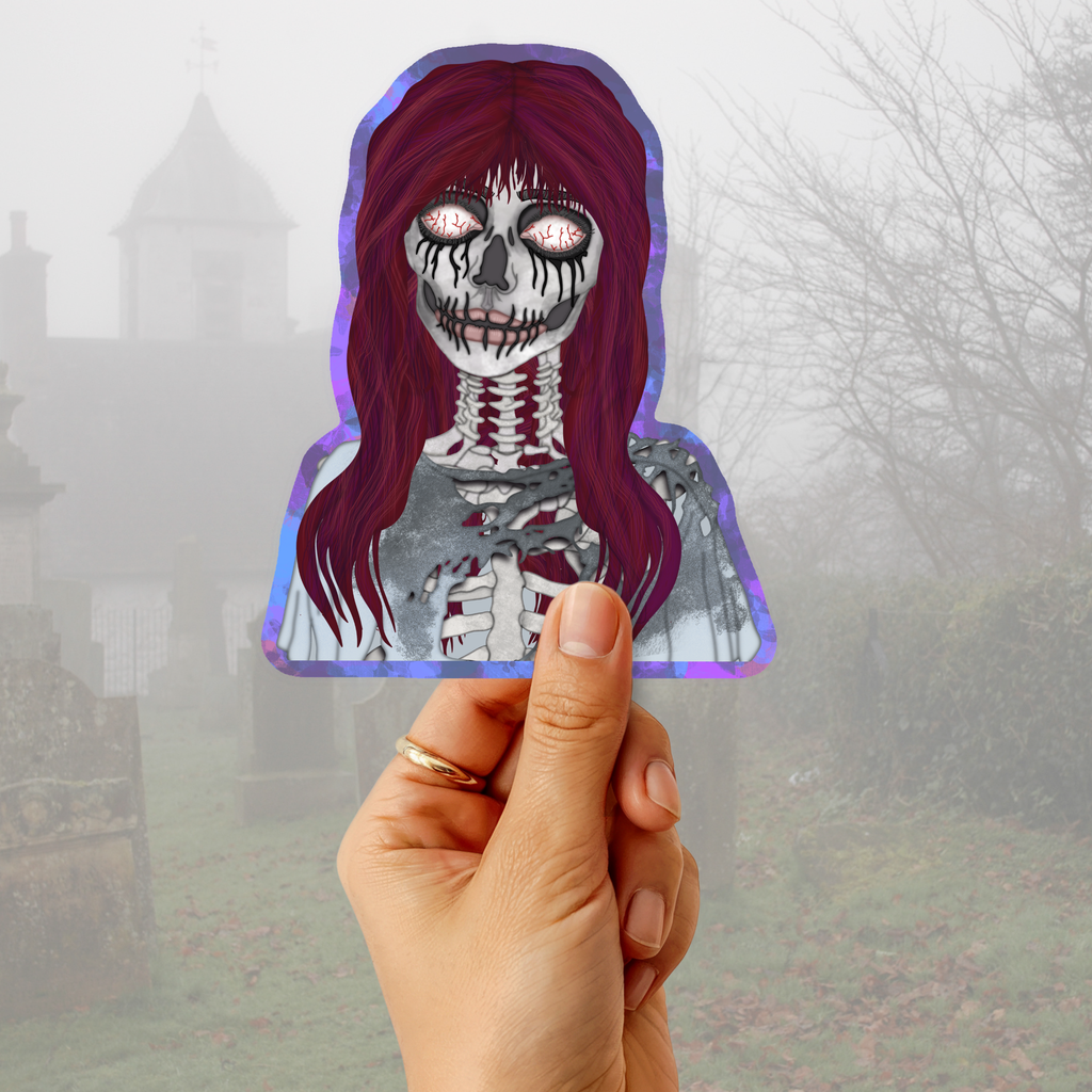 A hand holds a die-cut sticker featuring a stylized skeleton woman with long burgundy hair and glowing pink eyes, set against a foggy cemetery background.