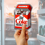 Hand holding a Diet Coke “Fridge Cig” sticker in front of an open refrigerator background.