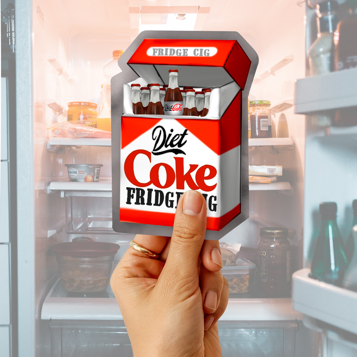 Hand holding a Diet Coke “Fridge Cig” sticker in front of an open refrigerator background.