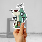 Hand holding a retro cartoon-inspired house sticker in front of an old television for a nostalgic 90s aesthetic mockup.