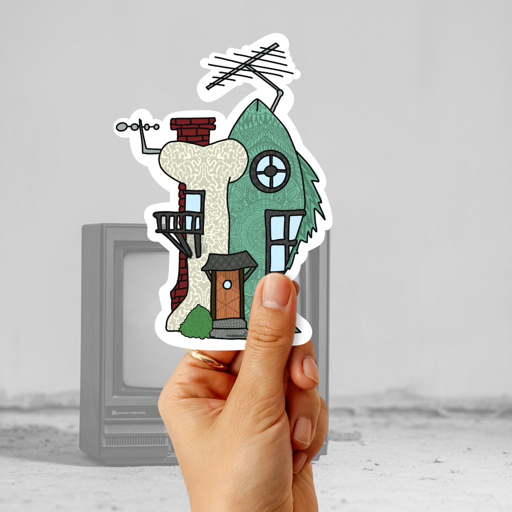 Hand holding a retro cartoon-inspired house sticker in front of an old television for a nostalgic 90s aesthetic mockup.