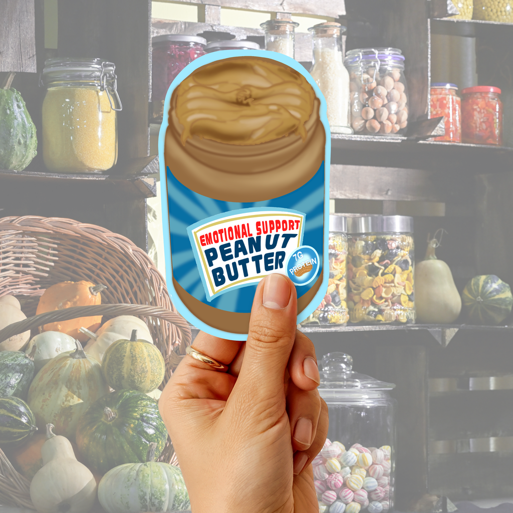 Hand holding an “Emotional Support Peanut Butter” sticker in front of a cozy pantry shelf background.
