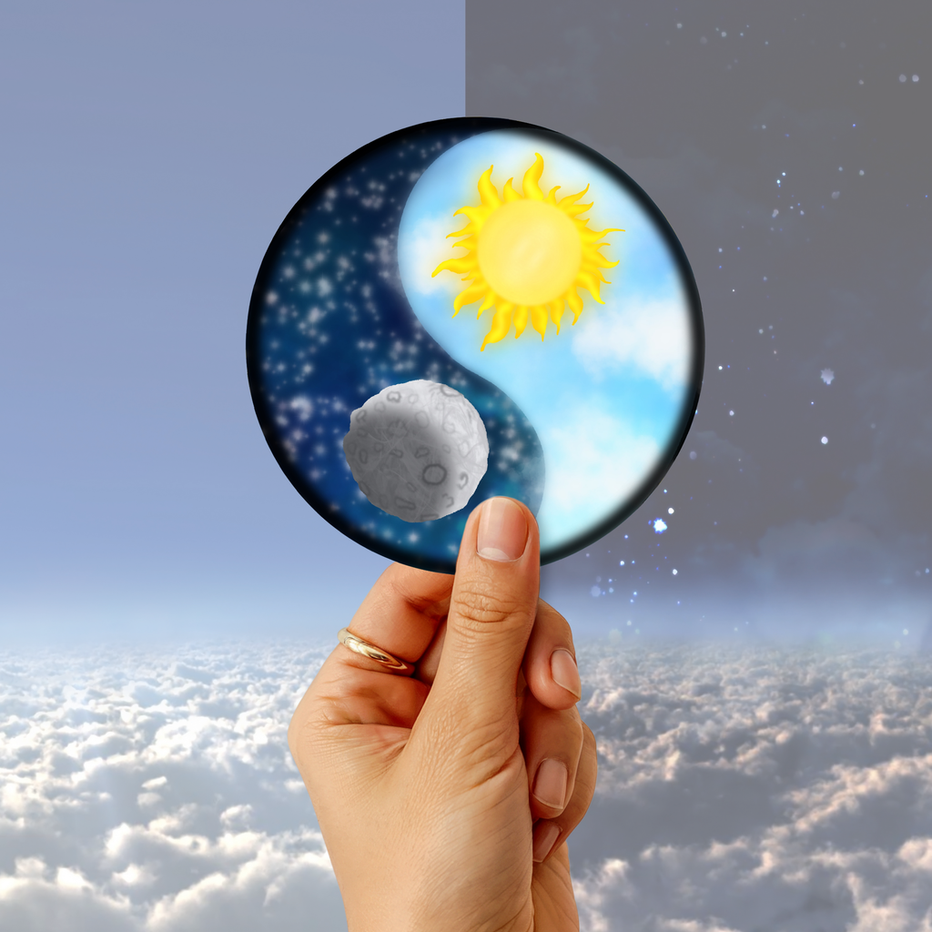 A hand holding a circular mirror or glass disc showing a yin-yang style design with a bright yellow sun, blue starry night side, and a gray moon, set against a sky-and-cloud background.