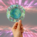A hand holding a die-cut sticker that reads 'ALL Panic No Disco' around a green and blue disco ball design, set against a pink and purple light-streaked gray background.