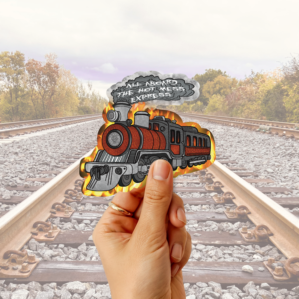 A hand holds a die-cut sticker featuring a cartoon steam locomotive with flames and a speech bubble that reads 'ALL NOBODY THE HOT METEOR EXPRESS' against a blurred railroad tracks background.