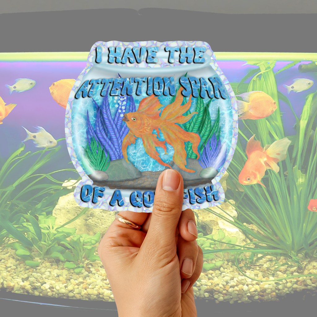 Hand holding a round sticker with a fishbowl design and text in front of an aquarium.
