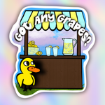 A die-cut sticker featuring a cartoon lemonade stand with the text 'Got Any Grapes?' in white bubble letters. The stand has a blue and yellow striped awning, a brown counter, a pitcher of yellow lemonade, two glasses, and a small yellow duck character standing at the bottom left.