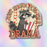 A die-cut sticker featuring a cartoon raccoon holding a popcorn bucket, with the text 'JUST HERE FOR THE DRAMA' in red marquee-style lettering, shown on a pastel iridescent background.