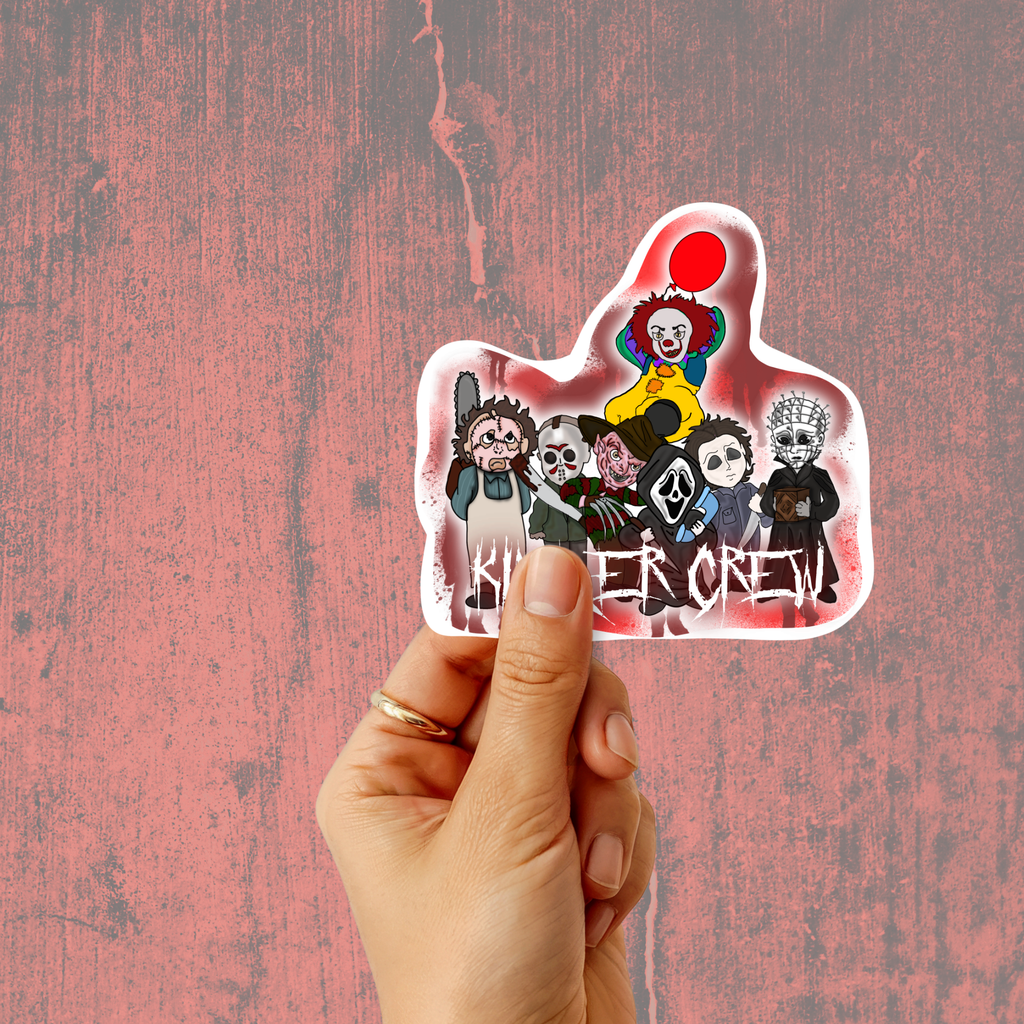 A hand holding a die-cut sticker featuring a group of horror movie villains, including Pennywise the Clown with a red balloon and the text 'Killer Crew', against a textured pink background.