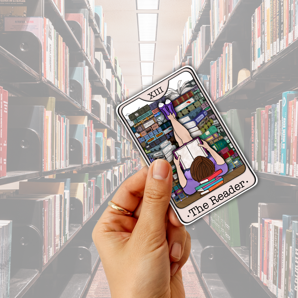 A hand holds a tarot card featuring an illustration of a person reading upside down in a library, with the text 'XIII The Reader' visible. The background shows blurred bookshelves in a library aisle.