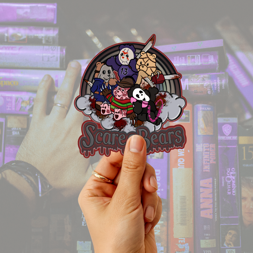 a hand holding an illustrated diecut sticker  featuring five cartoon bears in a horror-themed scene with knives, blood splatter, and the text 'Scare Bears' at the bottom. infront of a vintage vhs collections blurred out 