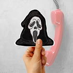 A hand holds a die-cut sticker featuring a black hooded ghost face design over a pink vintage telephone receiver against a light gray textured wall.