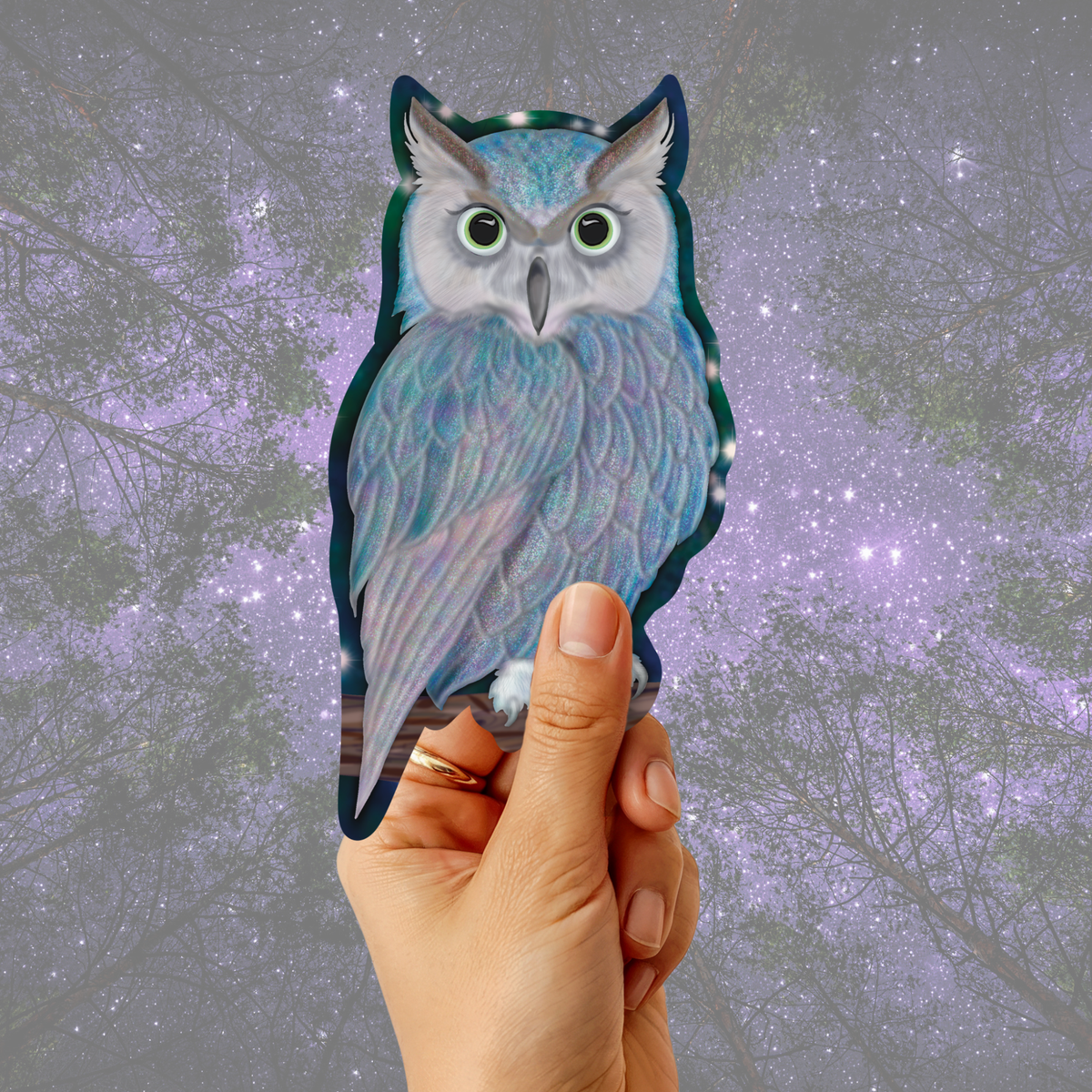 A hand holds a die-cut sticker of a detailed owl with iridescent blue, purple, and gray feathers against a blurred purple starry night sky background.