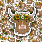 A die-cut sticker of a fluffy brown highland cow with white horns, wearing a floral sunflower crown, shown against a repeating patterned background of the same design.