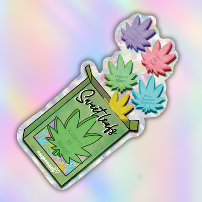 A die-cut sticker or decal featuring a green marijuana cigarette pack design with the words 'Sweet Leafs' and 'Kisses N UG S' on the wrapper, plus four colorful leaf-shaped pieces floating out in purple, green, pink, and blue. The item is photographed on a pastel iridescent background.