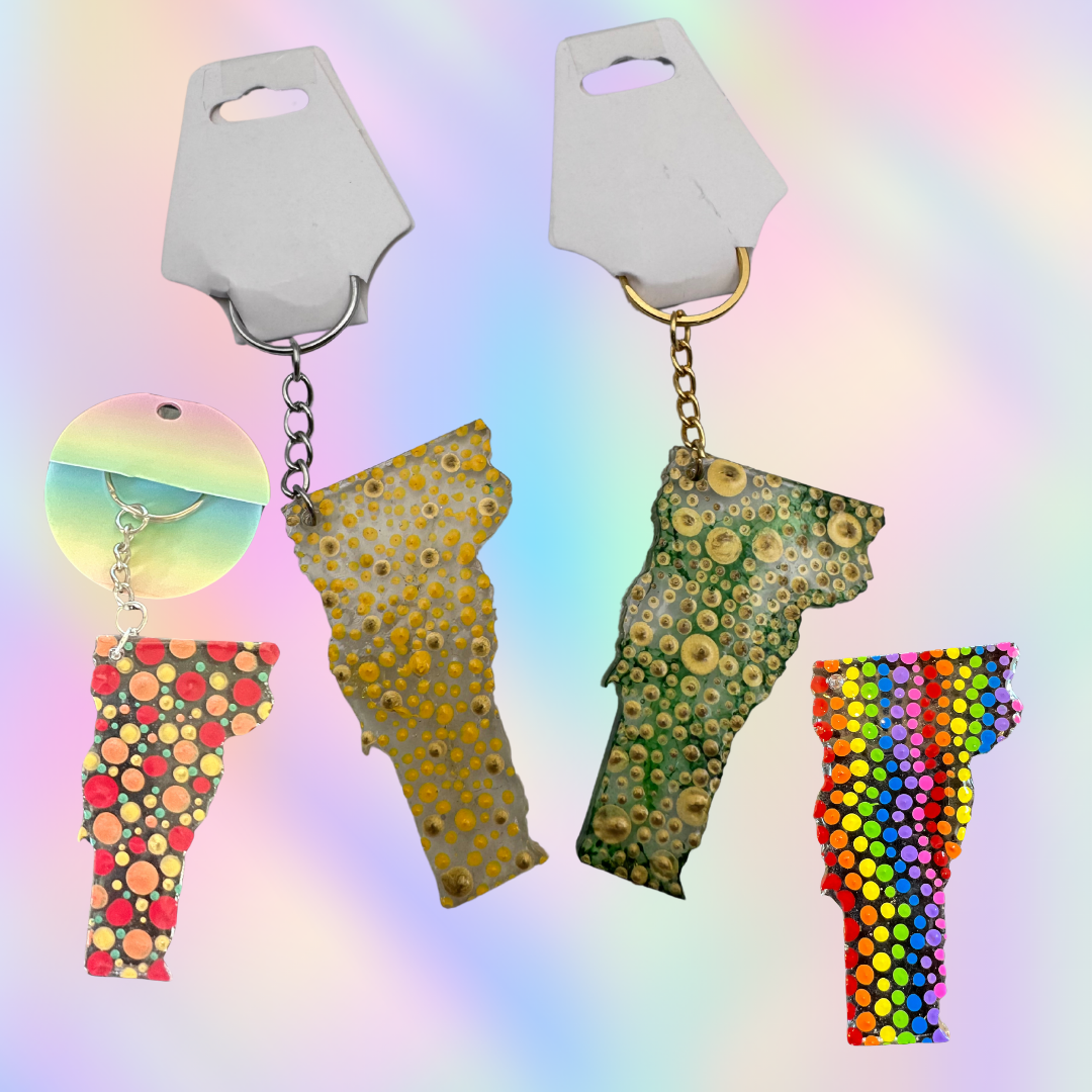 Four keychains shaped like the U.S. states of Vermont on a colorful gradient background.